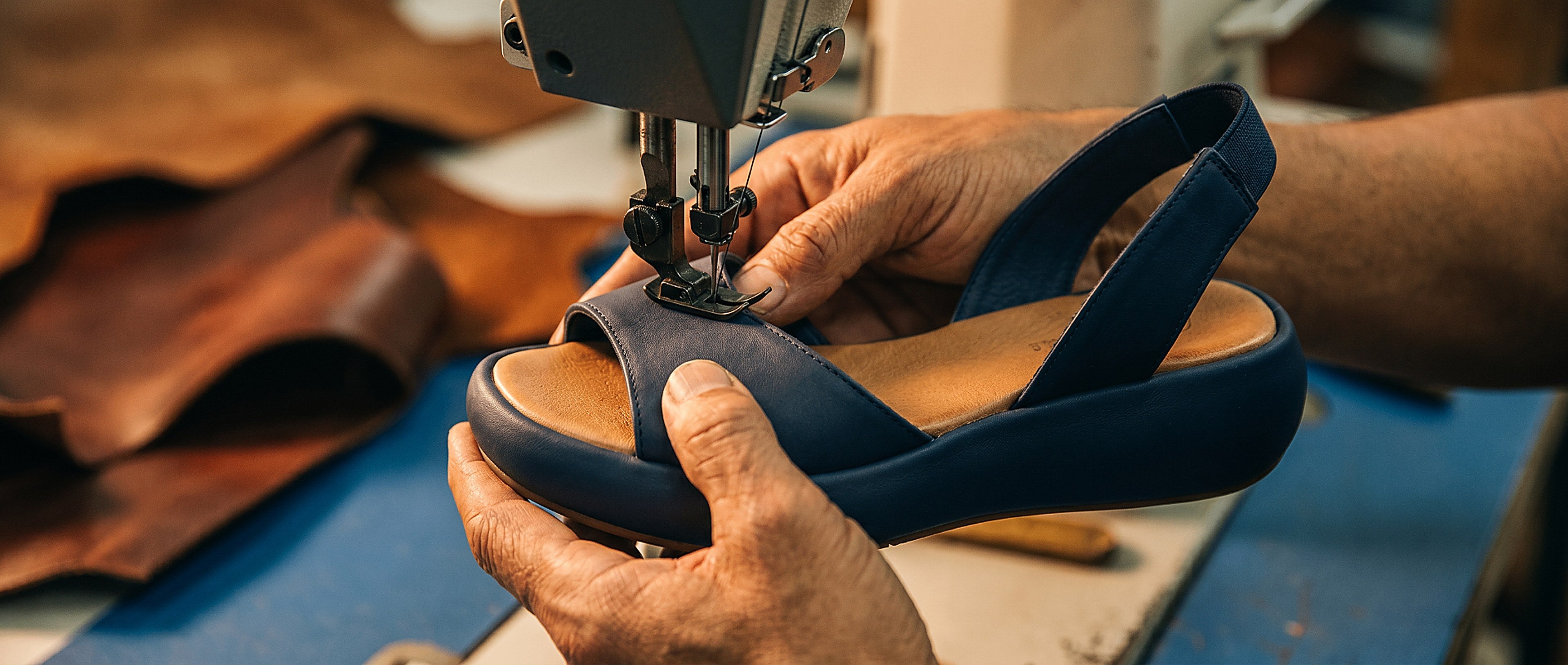 A craftsman stitching a navy leather sandal at a sewing machine